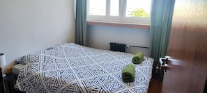 Ein Hotelzimmer mit Bett, Fenster mit Vorhängen, Heizkörper und Tür.