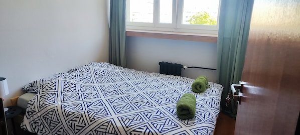 A hotel room with a bed, a window with curtains, a radiator, and a door.