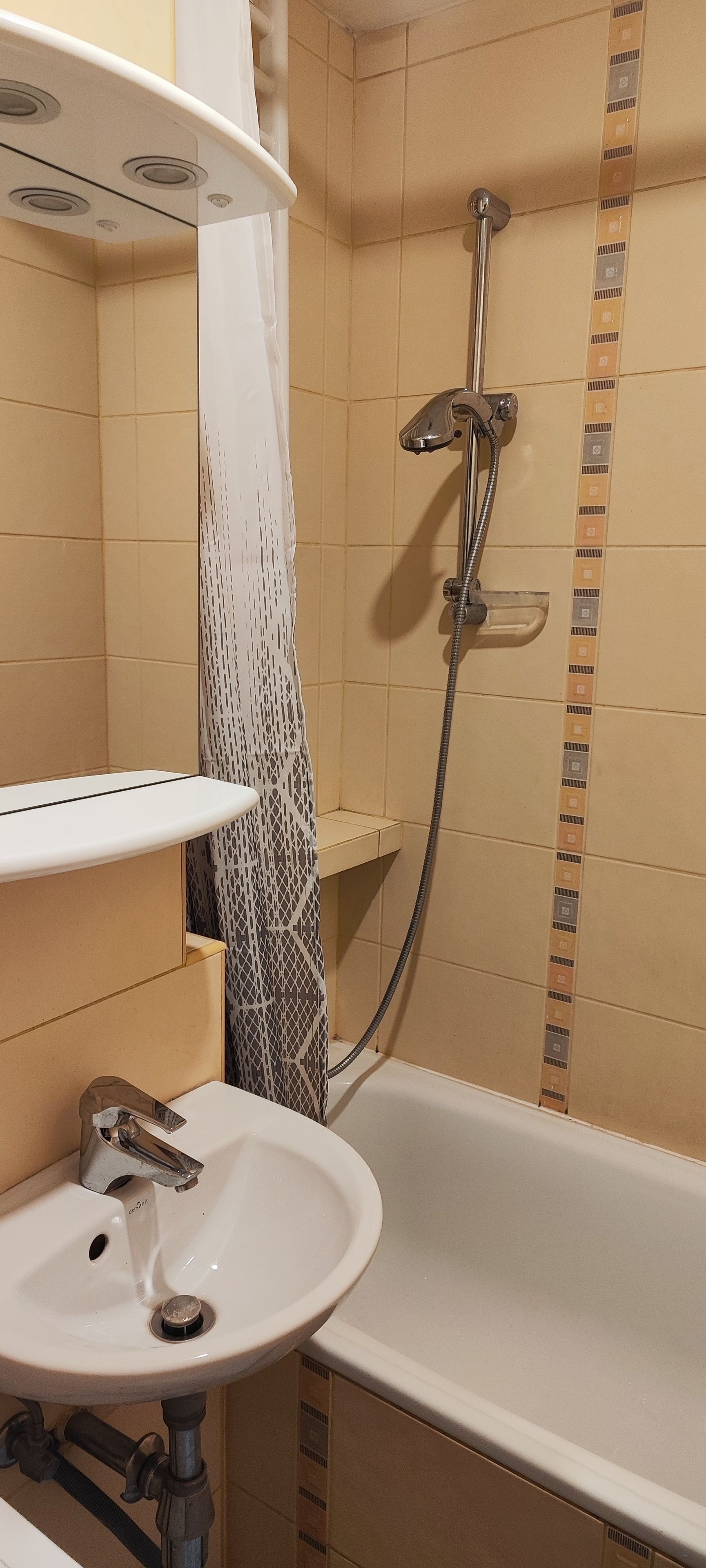 A bathroom with a white sink, a shower with a handheld showerhead, and tiled walls.