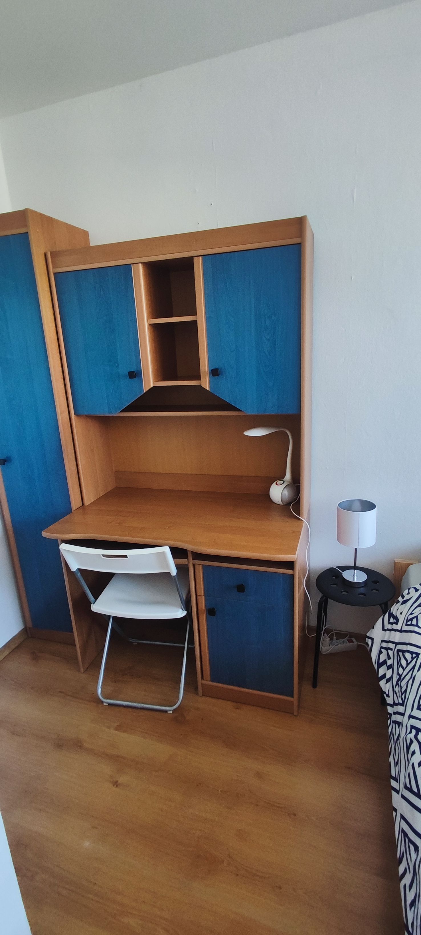 Ett kompakt skrivbord i trä med förvaringsfack och ett litet sidobord med en lampa.