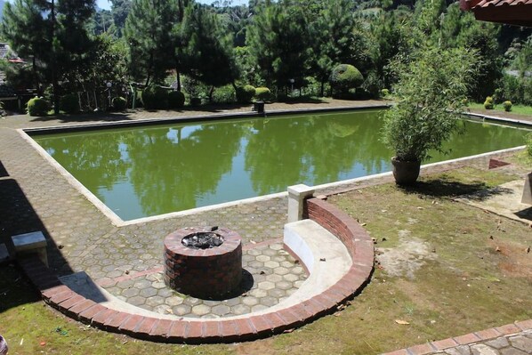 A rectangular pool with a brick fire pit in the center, surrounded by a brick border and a grassy area. - Villa Bayu Lembang (Lembang)