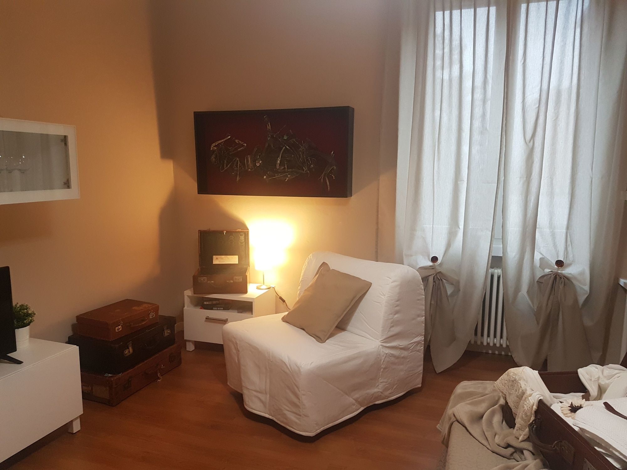 Una camera d'albergo con un letto, un comodino, una lampada, un quadro e una finestra con tende.