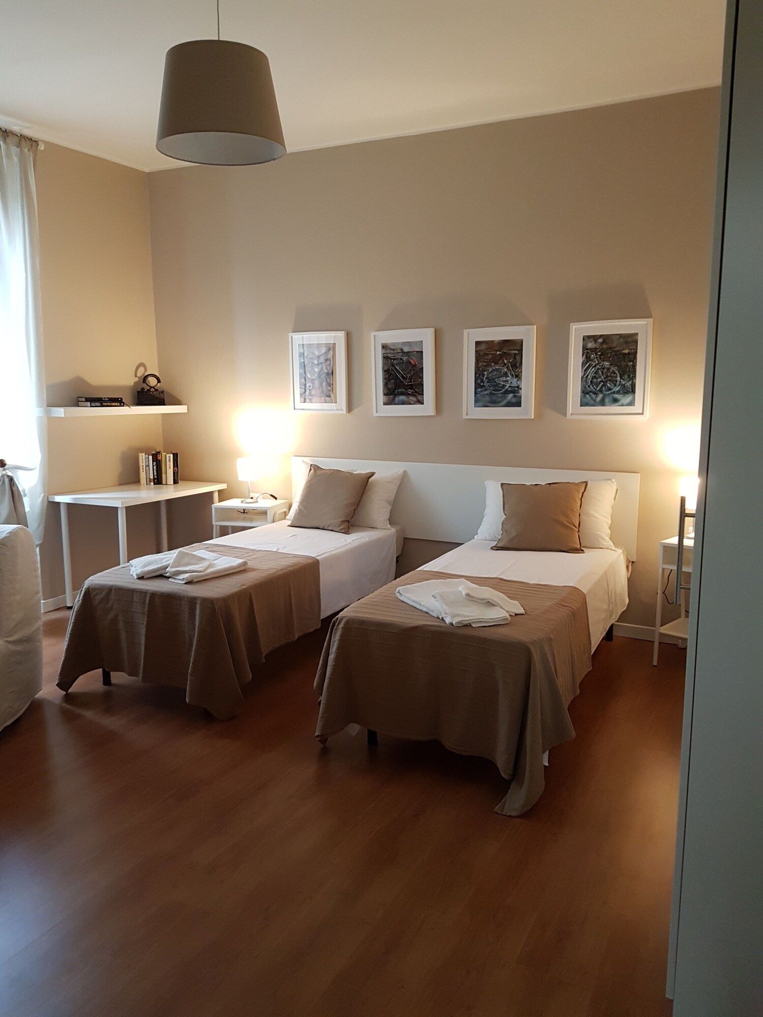 Camera d'albergo con due letti, una scrivania, una sedia e un lampadario.