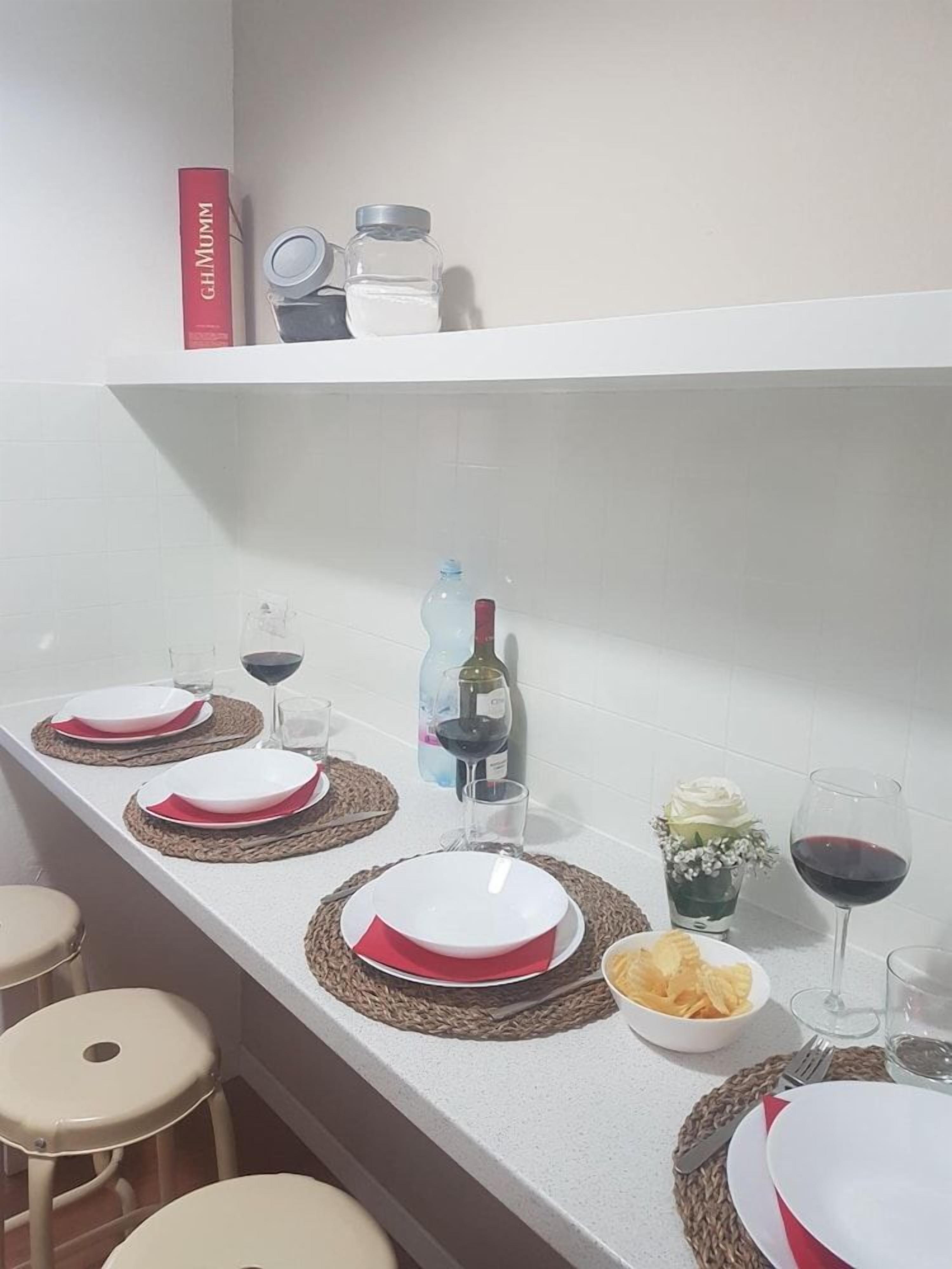 Zona pranzo con un piano di lavoro bianco, piatti bianchi e rossi, bicchieri da vino e una bottiglia di vino.