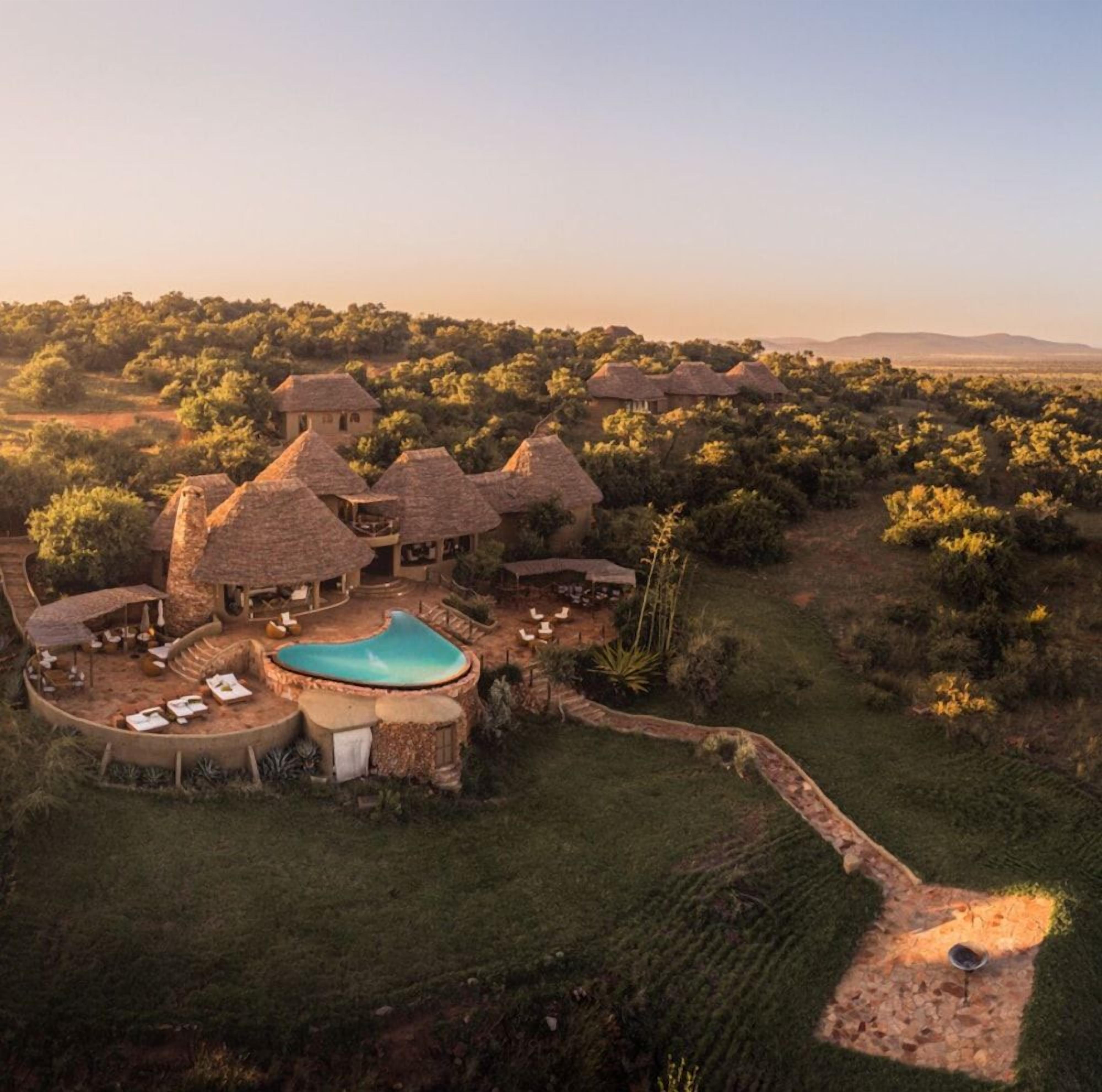 A resort with thatched-roof buildings, a swimming pool, and a surrounding landscape.