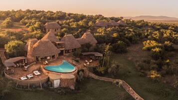 A resort with thatched-roof buildings, a swimming pool, and a surrounding landscape.