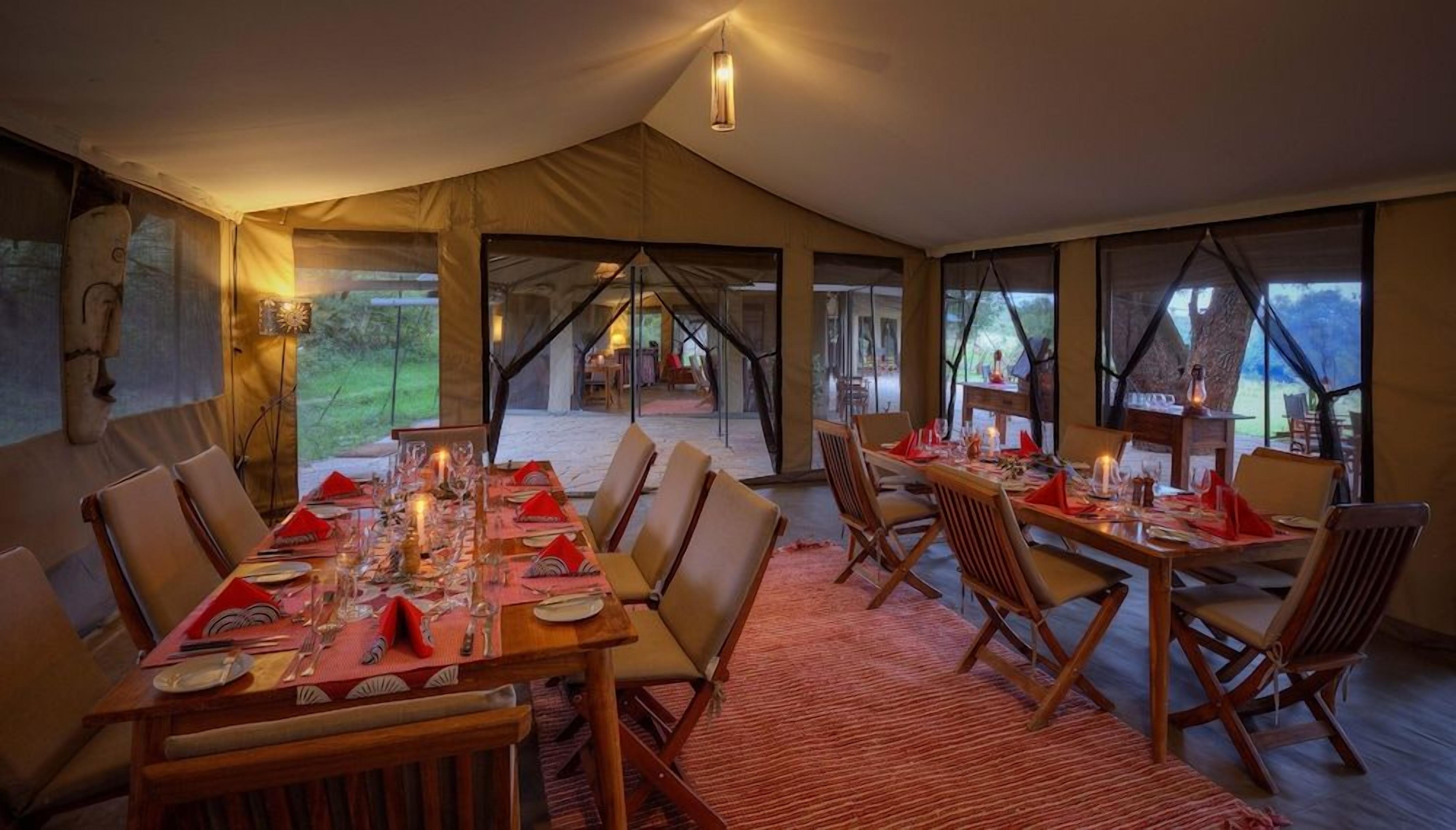 Un área de comedor con toldo, con mesas dispuestas para cuatro personas, decorada con velas y servilletas rojas.