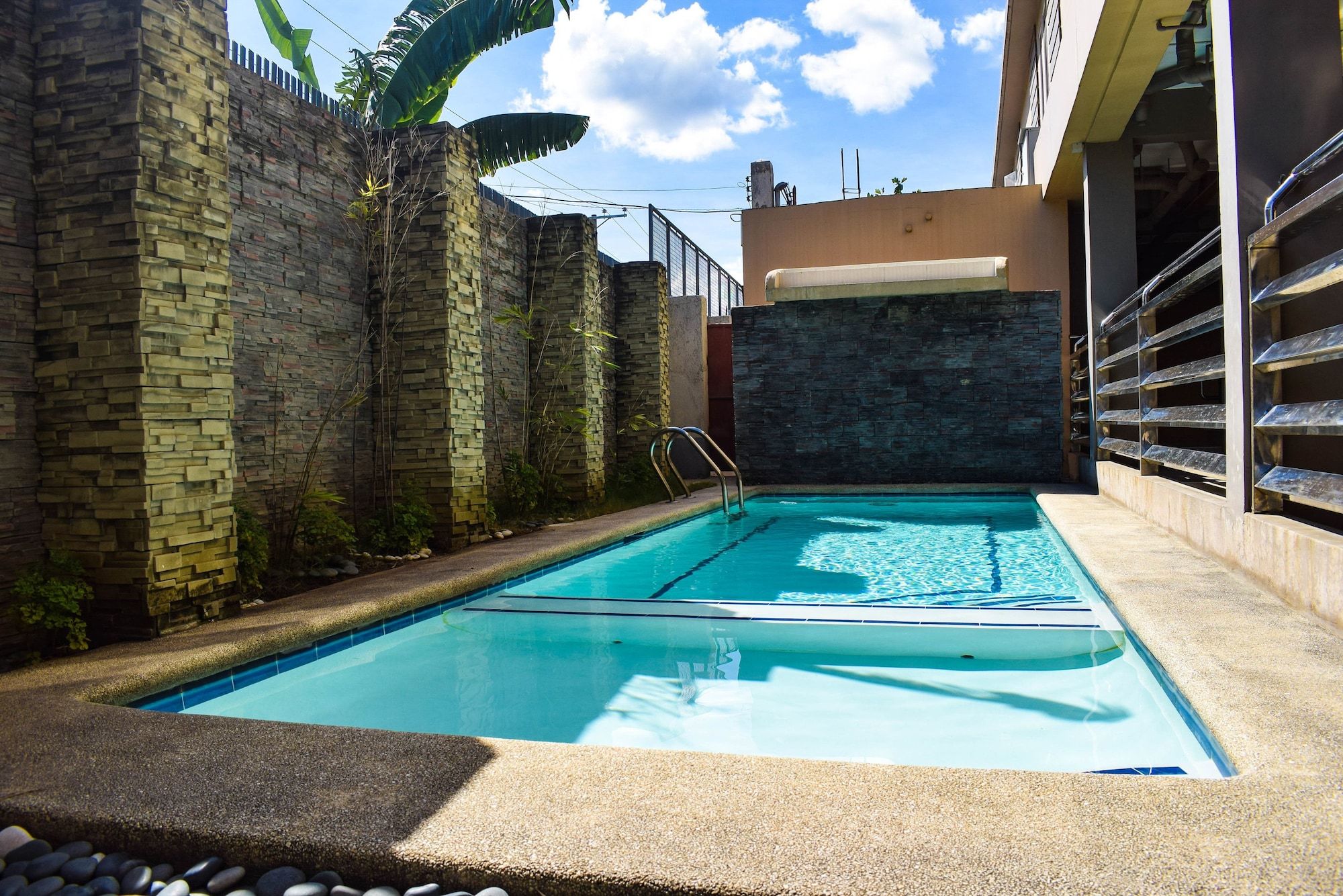 Piscina com parede de pedra e escada de metal.