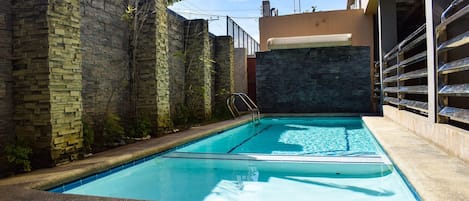 Piscina com parede de pedra e escada de metal.