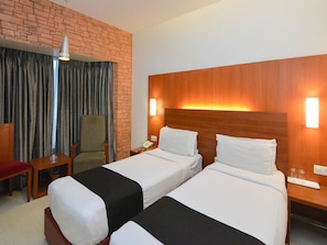 A hotel room with two beds, a brick accent wall, a wooden headboard, a desk with a chair, and a telephone. - Oyo Premium Deccan Apte Road (Pune)