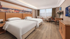 A hotel room with two beds, a desk, a chair, and a view of a cityscape. - Vienna International Hotel Guang'anmen (Beijing)