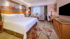 A hotel room with a large bed, a desk, a chair, a television, and a painting on the wall. - Vienna International Hotel Guang'anmen (Beijing)