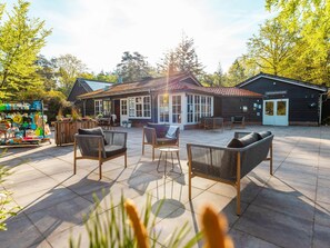 An outdoor patio area with wicker furniture, a covered seating area, and a building with a sign that reads 'Verkoopinformatie'. - Cabin in the Drenthe Countryside (Ruinen)