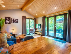 A modern living room with a wooden ceiling, large sliding glass doors to a garden, a flat-screen TV, and a dining area with a wooden table and chairs. - Cabin in the Drenthe Countryside (Ruinen)