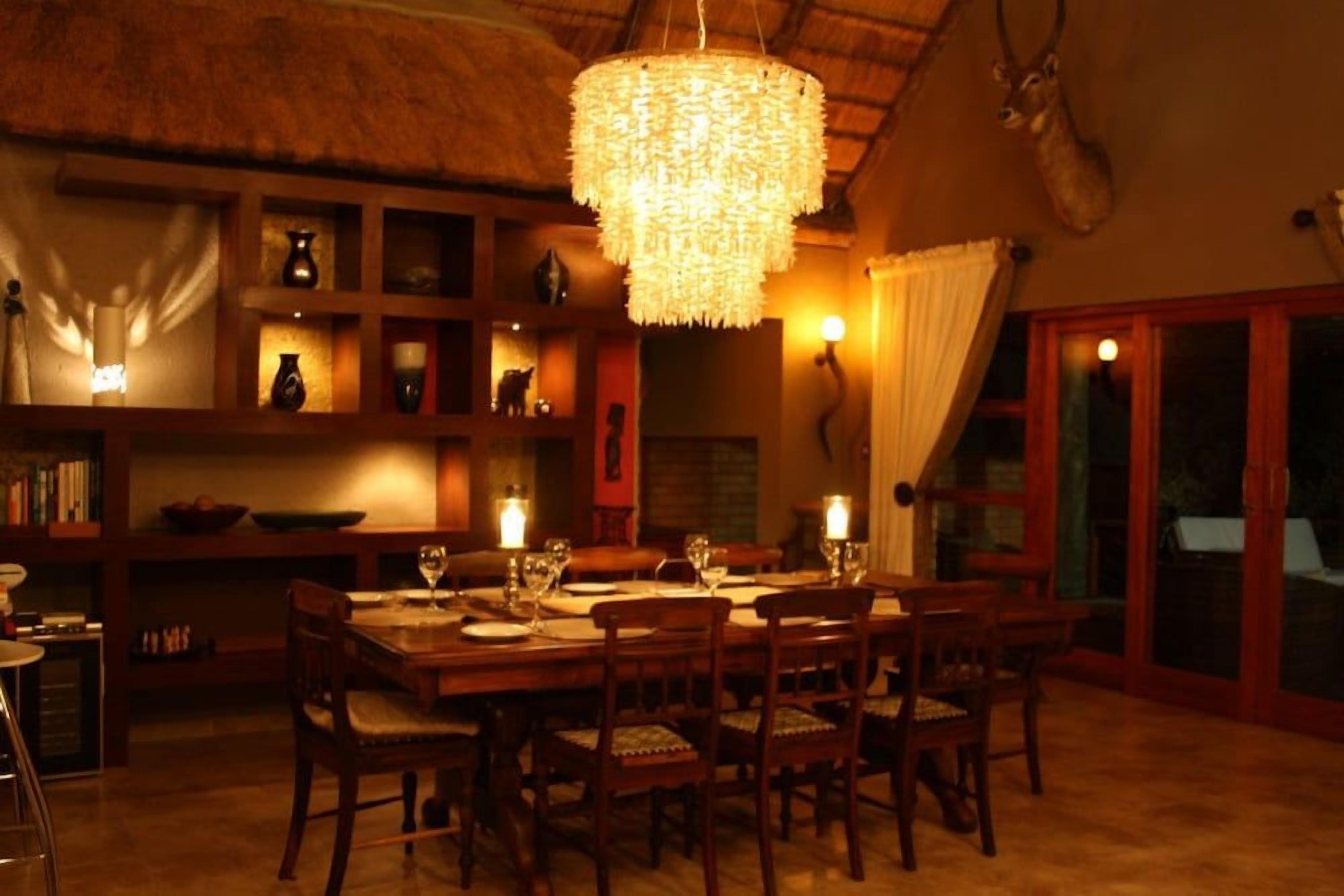 A dining area with a chandelier, wooden furniture, and a thatched ceiling.
