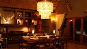 Un comedor con una gran mesa de madera dispuesta para seis personas, rodeada de sillas. Hay una araña colgando del techo, y una cabeza de venado montada en la pared.