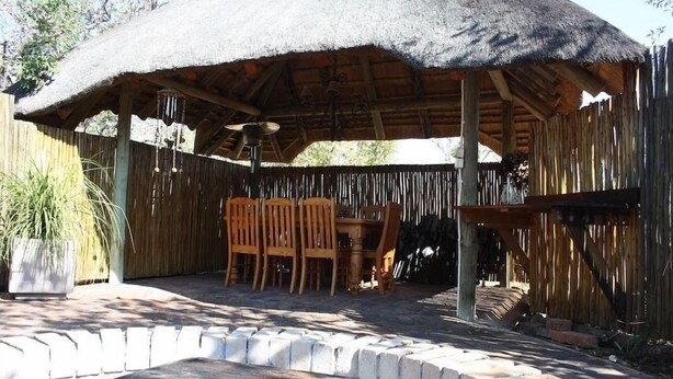 Un espacio de estar al aire libre cubierto, con mobiliario de madera y techo de paja.