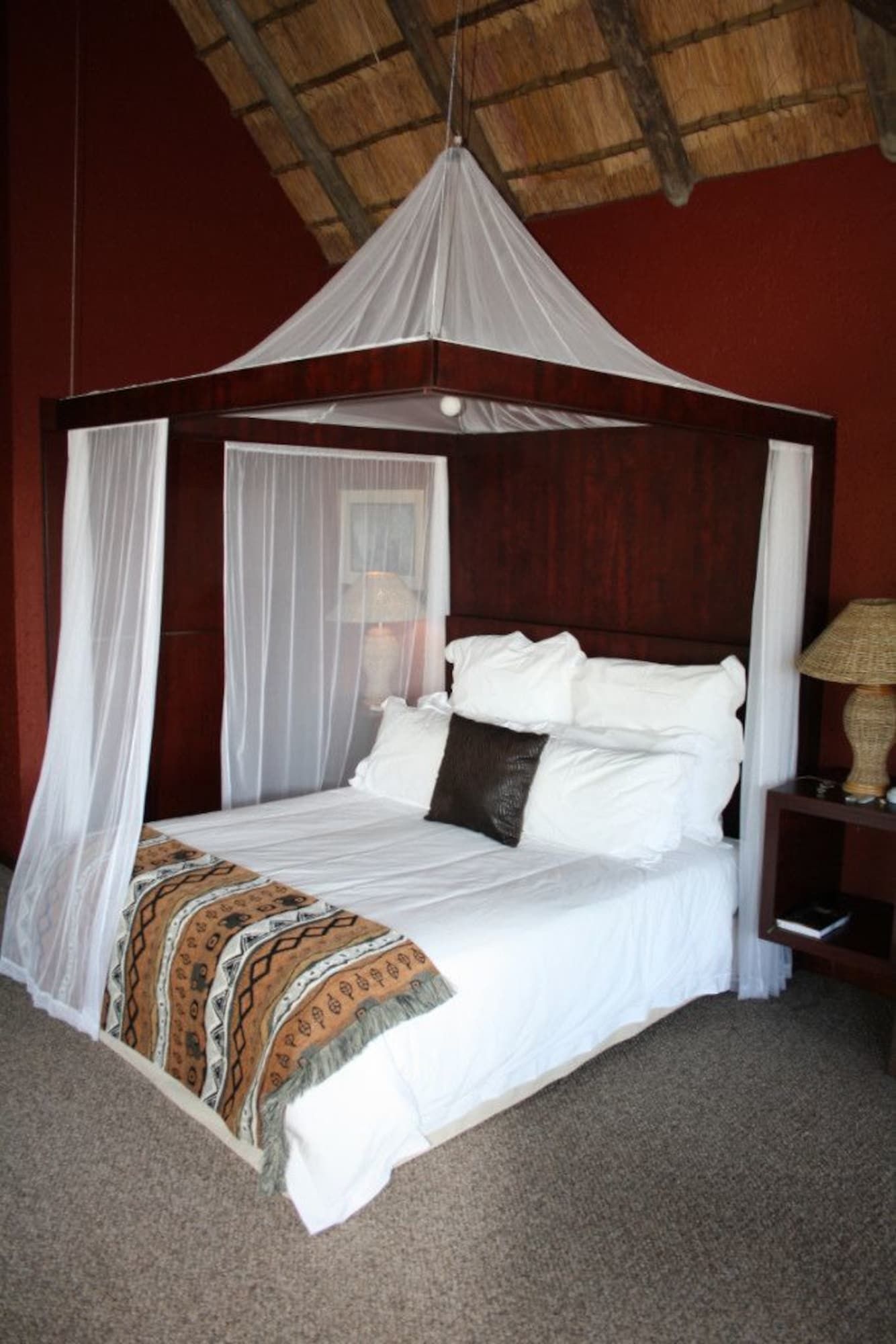 A four-poster bed with a canopy, white bedding, and a patterned throw blanket.