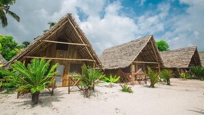 A row of thatched-roof huts with a sandy beach and palm trees in the foreground. - Jambo Beach Bungalows - Hostel (Paje)