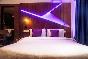 A hotel room with a bed, wooden panel walls, a wall-mounted light fixture, and a bathroom visible in the background. - Hôtel Villa Les Orchidées (Cotonou)