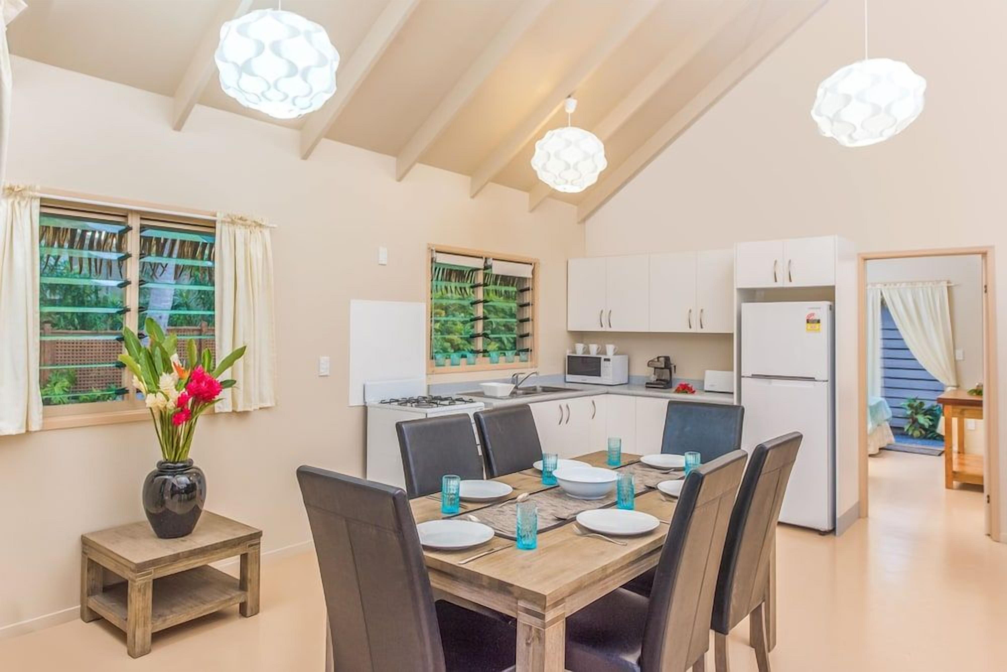 A modern kitchen with white cabinets, a dining table set for four, and a vase with flowers on a side table.