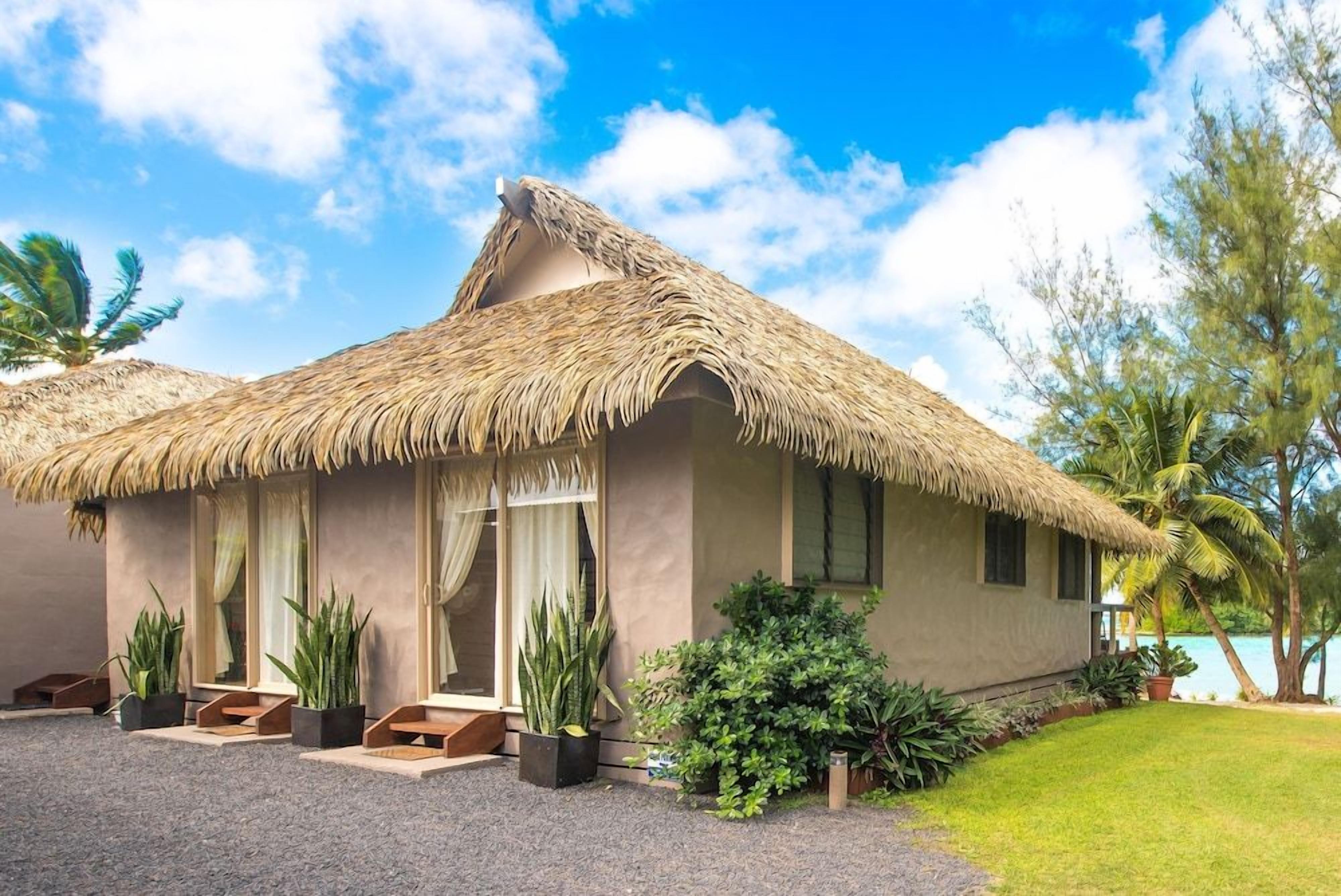A thatched-roof building with a paved entrance, potted plants, and a view of the sea.