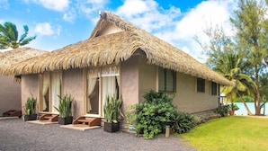 A thatched-roof bungalow with a paved driveway, potted plants, and a view of the ocean. - Muri Lagoon Villa (Rarotonga)