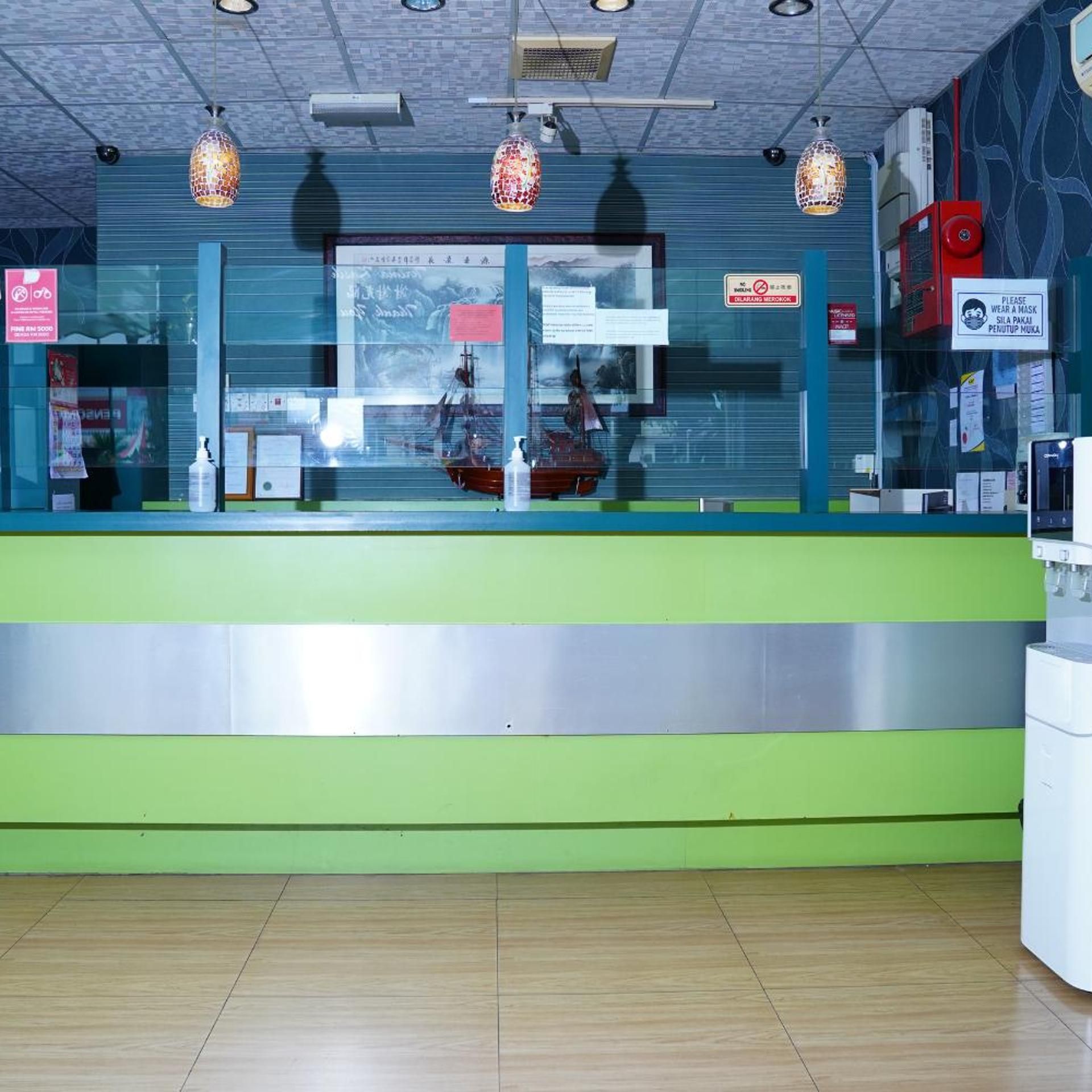 Zona de recepción con un mostrador verde, un modelo de barco y un cartel solicitando el uso de mascarillas.