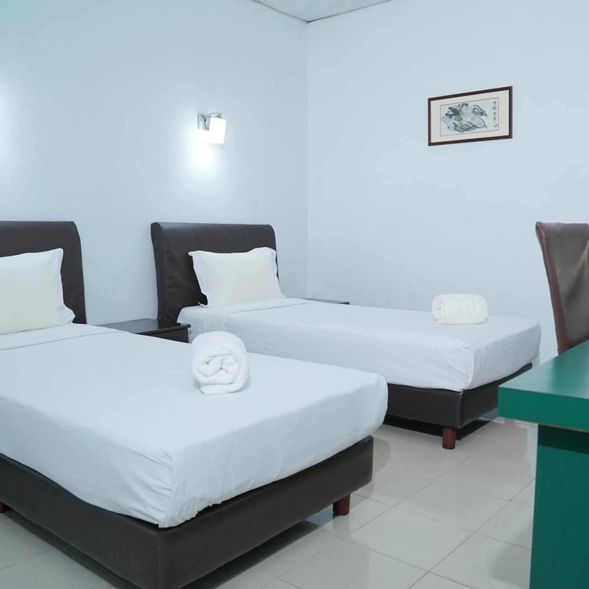 A hotel room with two beds, a desk, and a wall-mounted light.