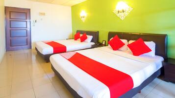 A hotel room with two beds, each with a red and white bedspread and matching pillows. There are wall-mounted light fixtures and a door visible.