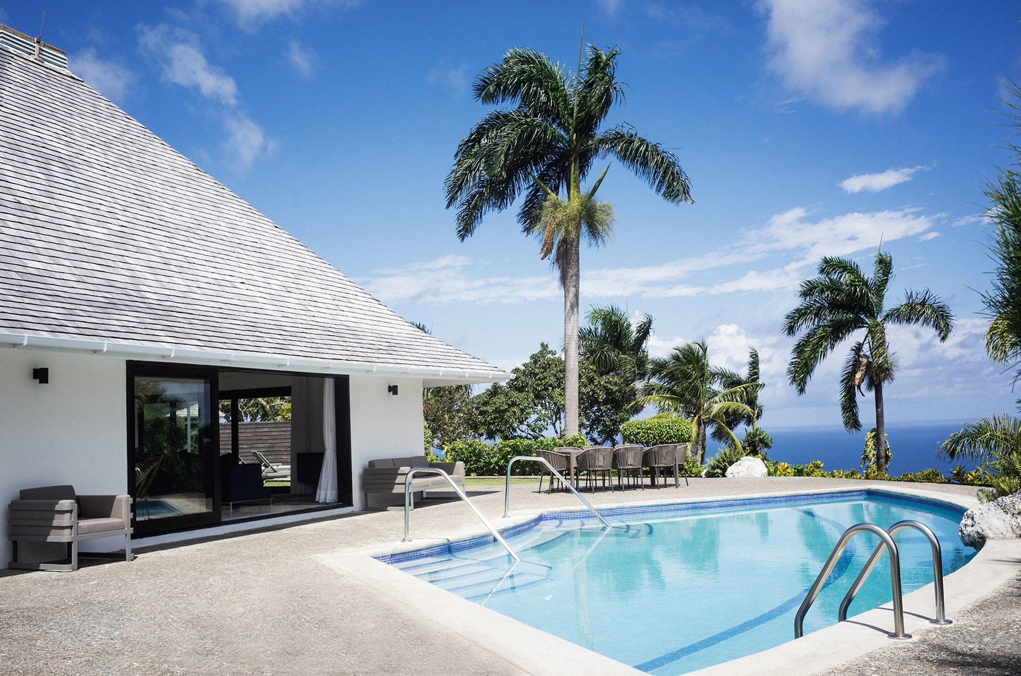 A modern building with a swimming pool, outdoor seating, and palm trees.
