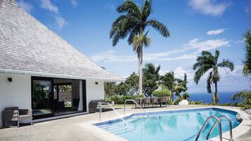 A modern building with a swimming pool, outdoor seating, and palm trees.