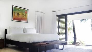 A bedroom with a bed, a bedside table, a framed poster, and a view of palm trees through a window.