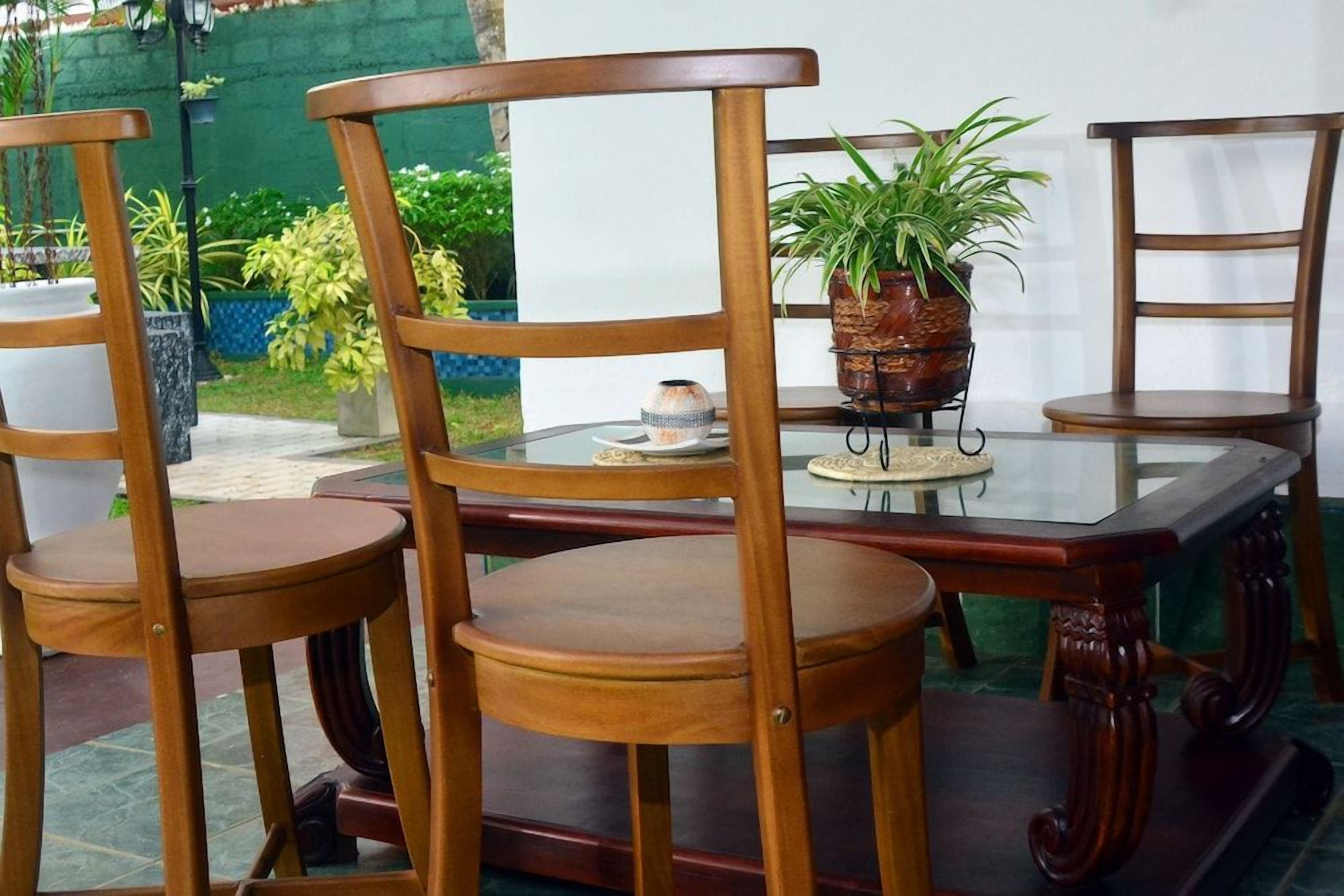 Een eethoek met een glazen tafel, omringd door houten stoelen, een potplant en een decoratieve schaal.