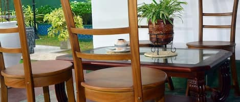 A dining area with a glass table surrounded by wooden chairs, a potted plant, and a decorative bowl.