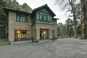 A two-story stone building with green-framed windows and a porch with seating. - Brij Villa, Dalhousie (Dalhousie)
