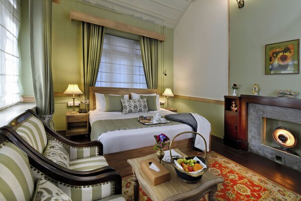 A hotel room with a bed, two bedside tables, a sofa, a table with a fruit basket, a fireplace, and a painting on the wall. - Brij Villa, Dalhousie (Dalhousie)