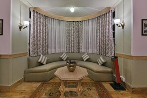 A corner living room with a curved sofa, a small table, and a patterned rug. - Brij Villa, Dalhousie (Dalhousie)