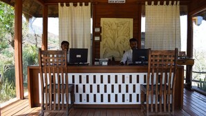 A reception desk with two individuals seated behind it, a check-in/out sign, and a decorative wall panel.