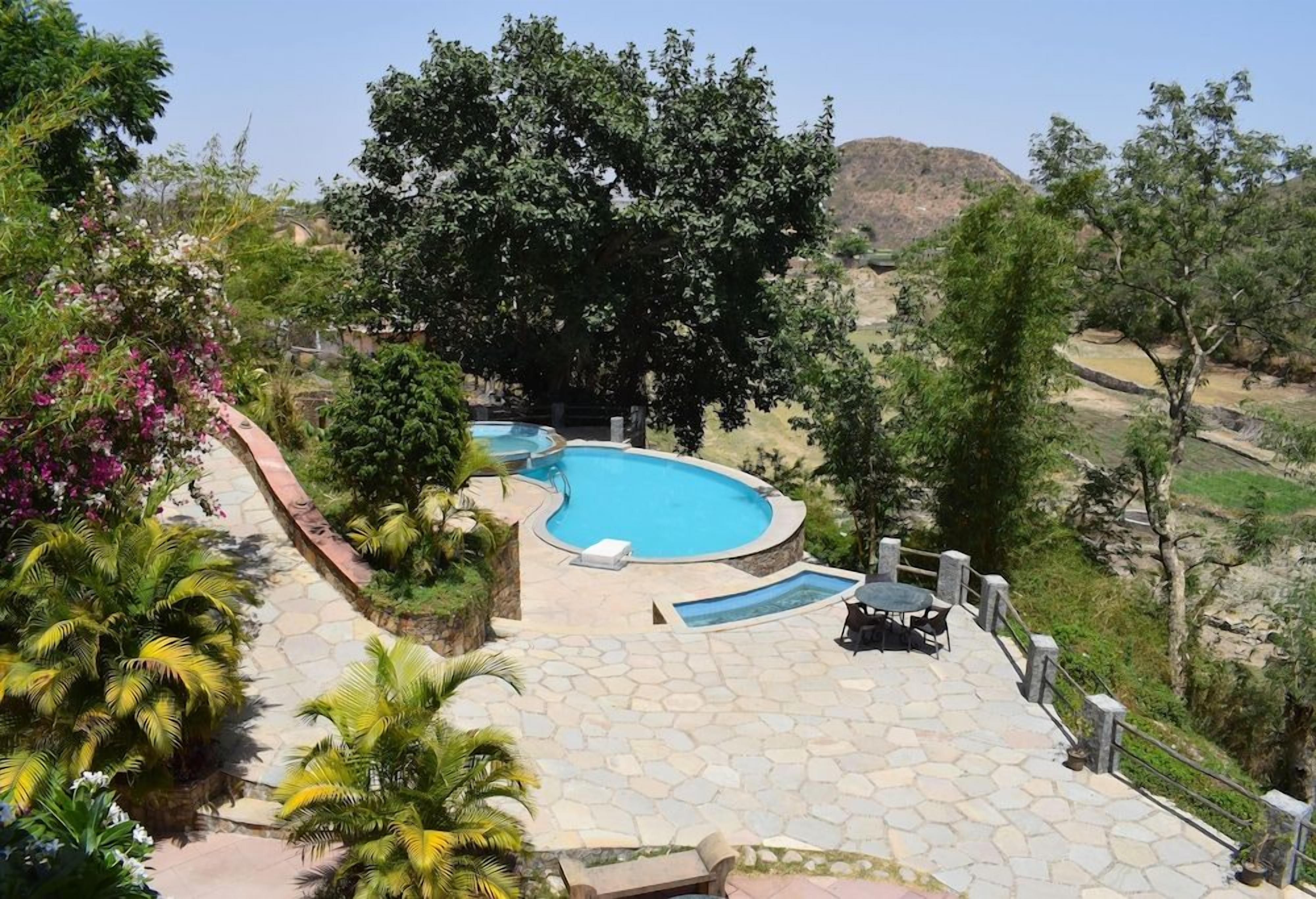 A swimming pool with a stone deck, surrounded by lush greenery and trees.