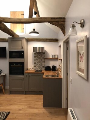 A compact kitchen with built-in appliances, a wooden ceiling, and a small dining area.