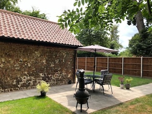 A patio with a brick wall, a barbecue grill, outdoor furniture, and potted plants. - Rivers Rest (Norwich)