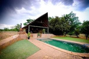 A pool area with a covered seating area and a brick patio.