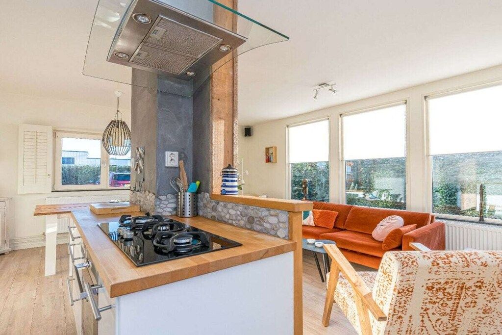Eine moderne Küche mit einer zentralen Kochinsel, einer Wand mit Steinverkleidung und Blick ins Freie durch große Fenster.