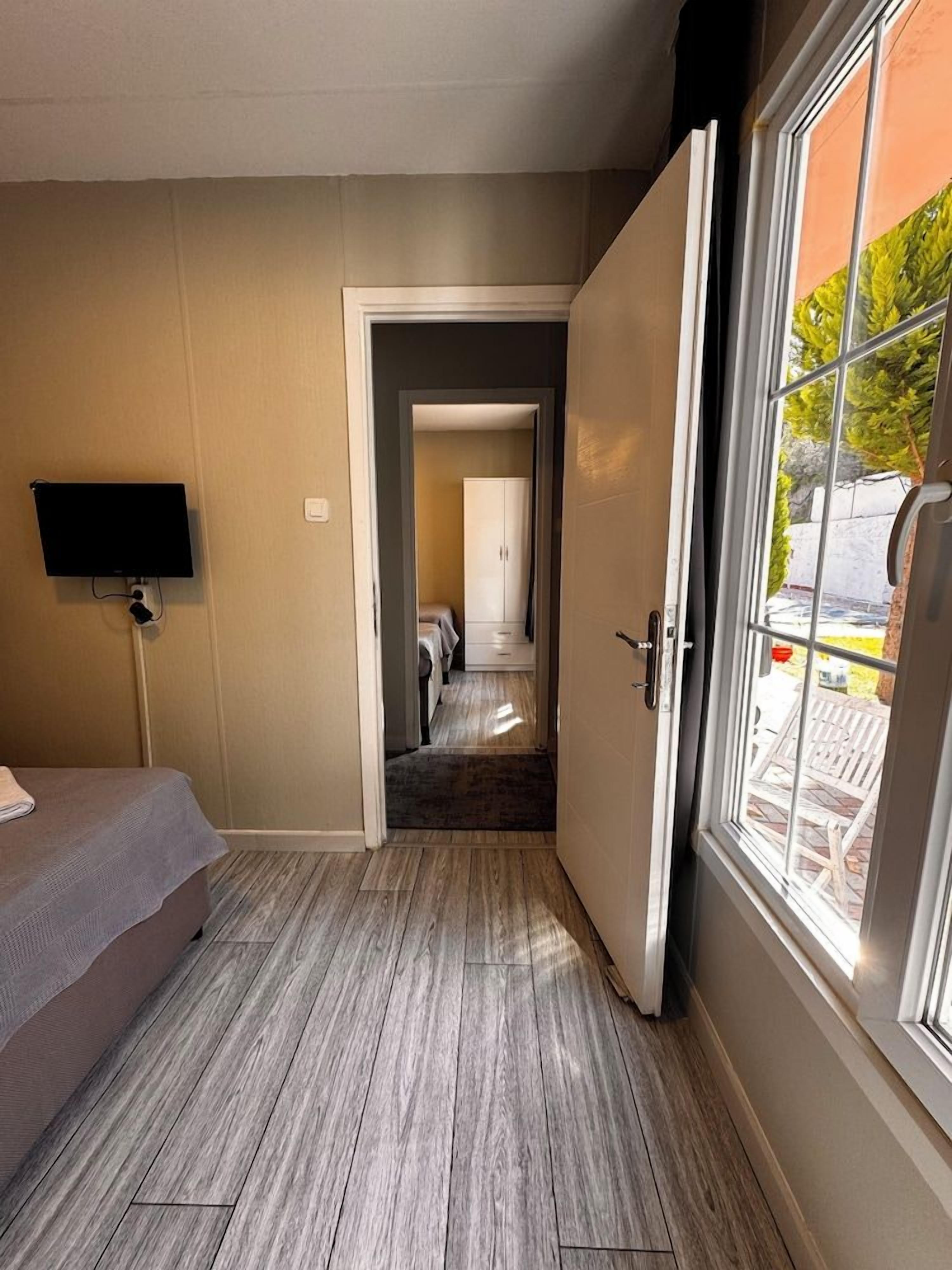A hotel room with a bed, a television, and a door leading to a hallway with a view of the outside.