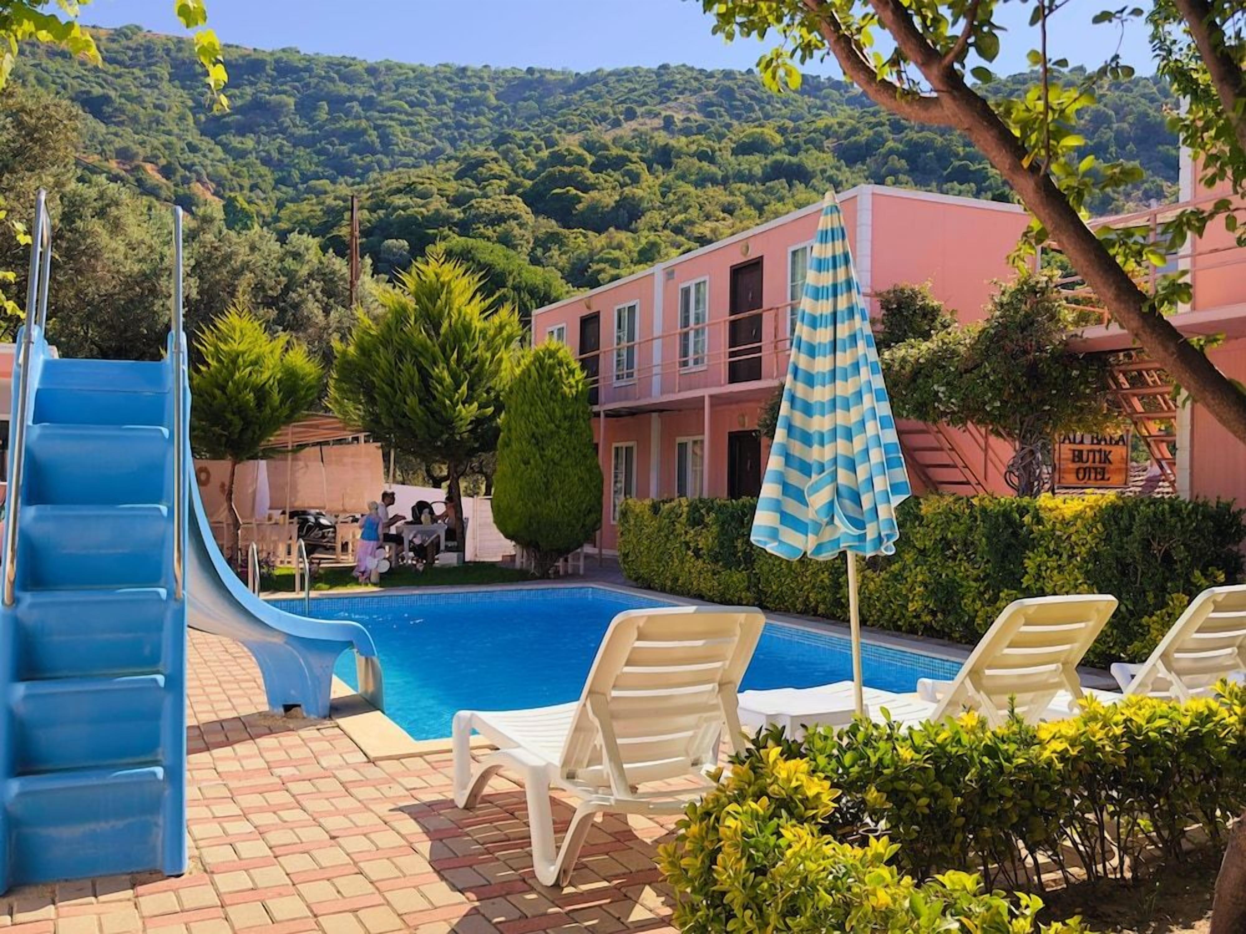 A pool area with a blue slide, lounge chairs, and a building with a sign.