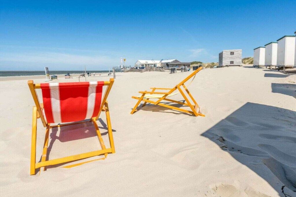 Two beach chairs on a sandy beach with a clear sky.