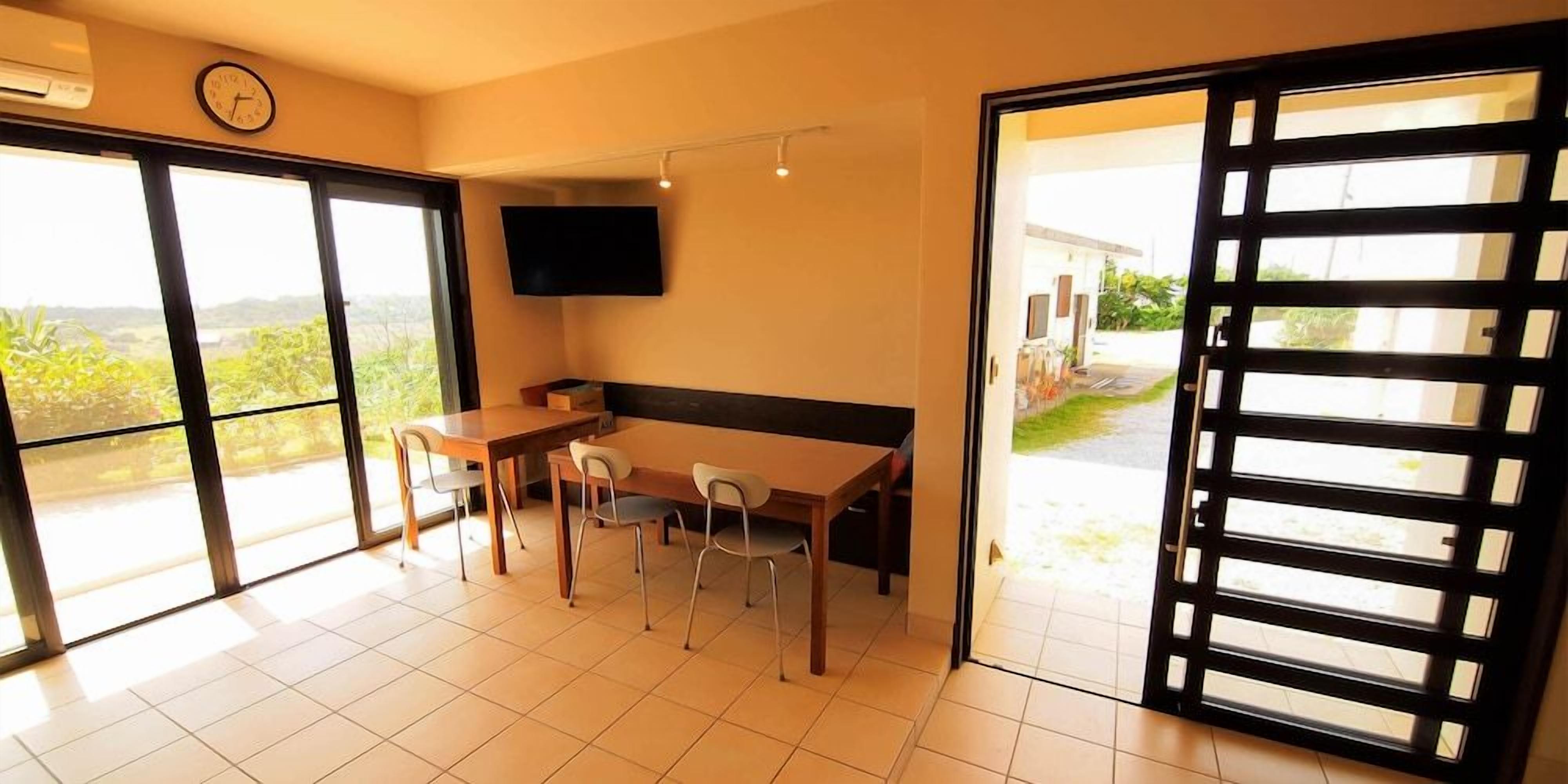 A room with a dining table, chairs, a flat-screen TV, and a sliding glass door leading to a balcony.