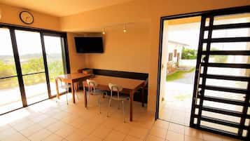 A room with a dining table, chairs, a flat-screen TV, and a sliding glass door leading to a balcony.