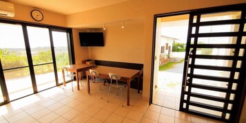 Una habitación con una mesa de comedor, sillas, un televisor de pantalla plana y un ventanal corredero que da a un balcón.